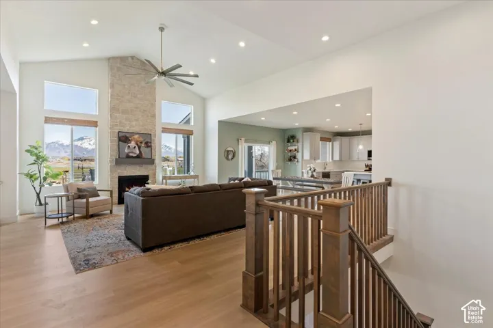 Vaulted ceilings with recessed lighting, full-height stone fireplace, wood-finish flooring, and wooden staircase railing