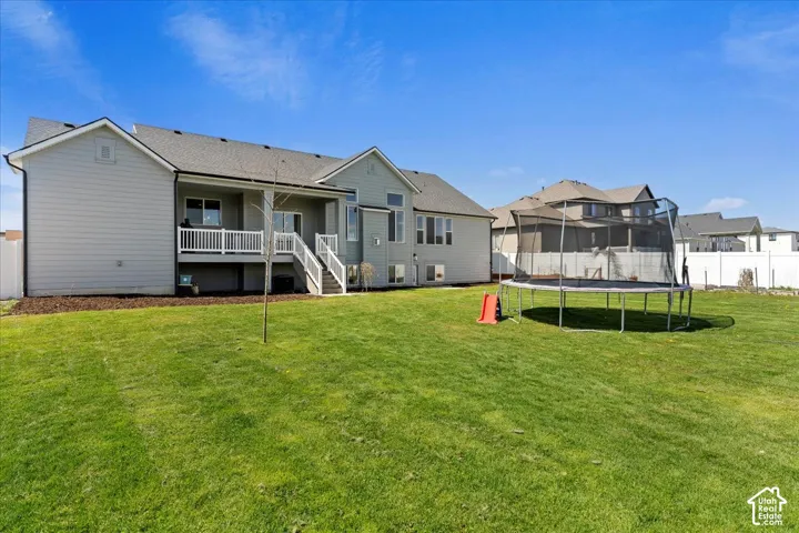 Rear exterior featuring horizontal lap siding, an elevated deck with white railing, and a fenced backyard with lawn space