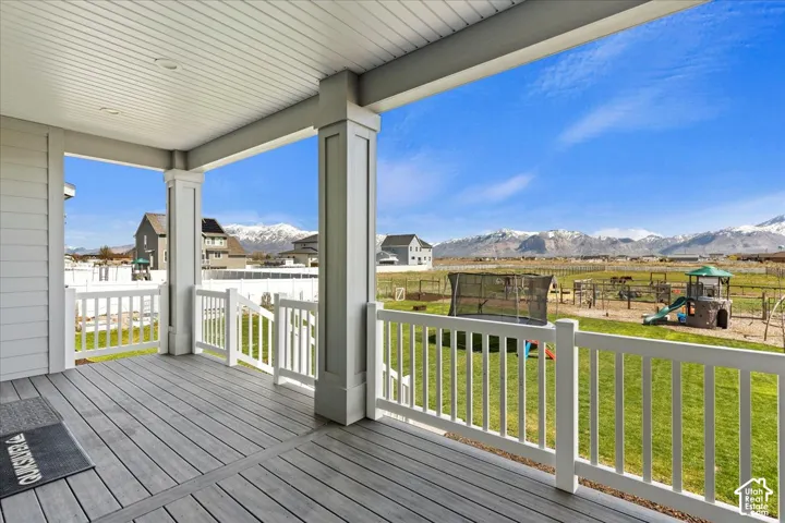 Covered patio featuring composite decking, white structural columns, white railings, and mountain scenery