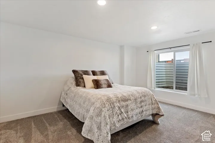 Neutral wall-to-wall carpeting, recessed ceiling lighting, and a window with a corrugated metal egress well