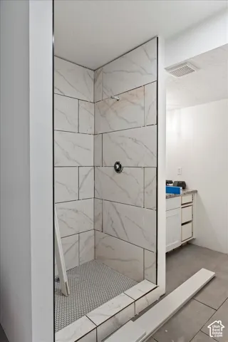 Shower enclosure featuring large-format tile surround with vein detailing, mosaic-tiled flooring, and metal shower fixture