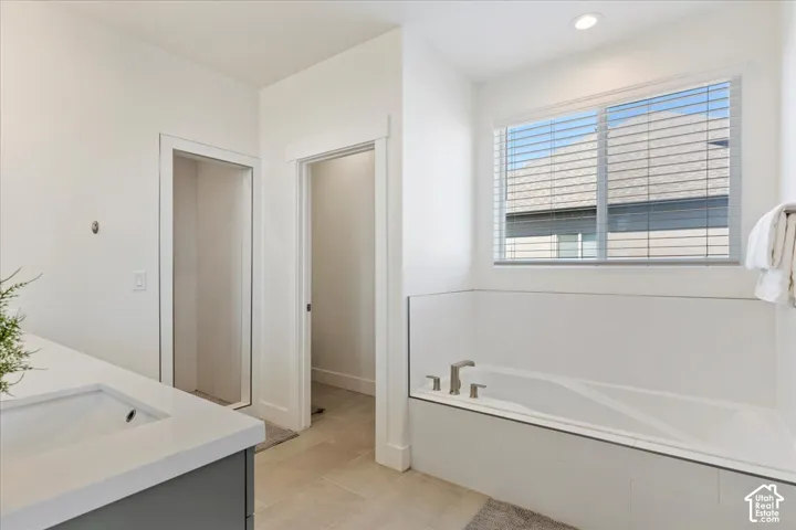 Soaking tub featuring a tiled surround and glass partition, neutral-toned tile flooring, recessed ceiling lighting, and a quartz-topped vanity
