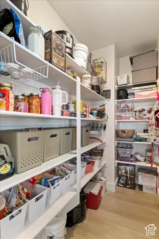 Walk-in pantry featuring white shelving, horizontal shiplap-style wall detailing, and light-toned wood-finish flooring