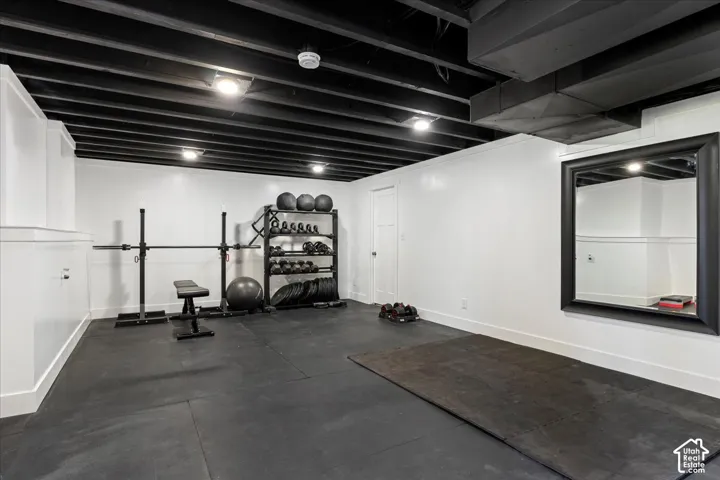 Finished room featuring an open-joist ceiling, smooth white walls, recessed lighting, and rubberized flooring