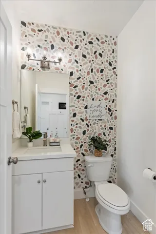 Bathroom featuring a terrazzo-patterned accent wall, white cabinetry with a solid-surface countertop, wood-finish flooring, and a wall-mounted multi-light fixture