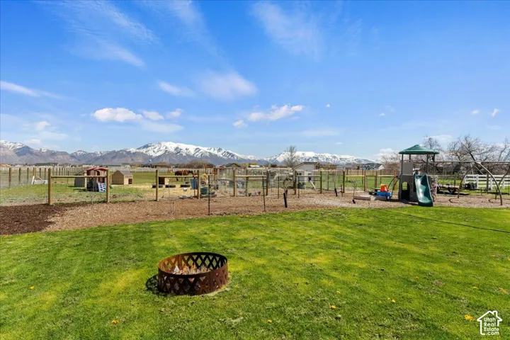 Expansive outdoor space featuring a manicured lawn, a metal fire pit, post-and-rail fencing, and prominent mountain backdrops