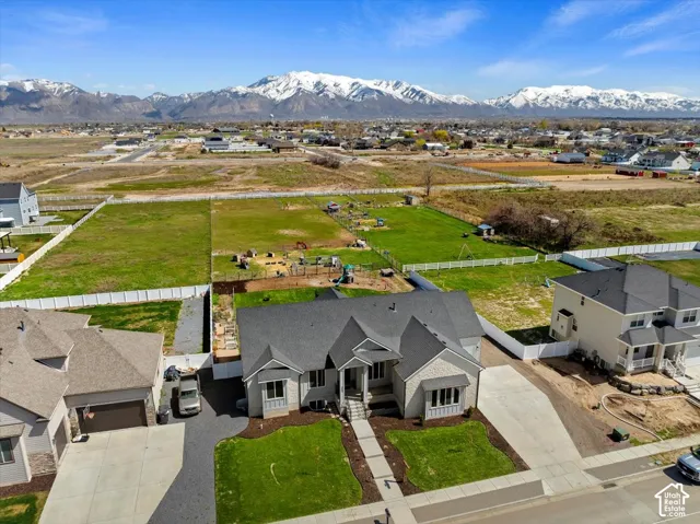 Multi-gabled exterior featuring light-toned siding and stone masonry, concrete driveway, white vinyl fencing, and expansive grounds set against a mountain backdrop