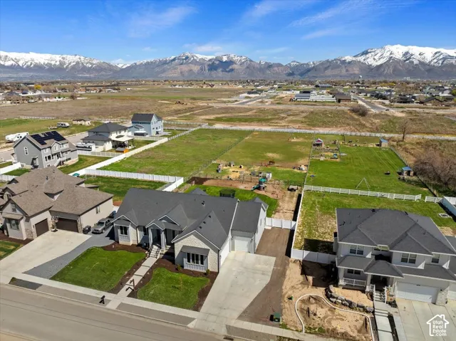 Aerial perspective of a multi-story residence with a multi-gabled roof, stone and siding facade, attached garage, concrete driveway, and expansive lot with mountain backdrop