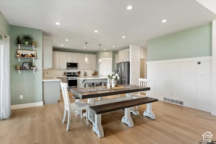 Kitchen featuring a central island with integrated seating, shaker-style cabinetry, stainless steel appliances, wood-finish flooring, and wainscoting