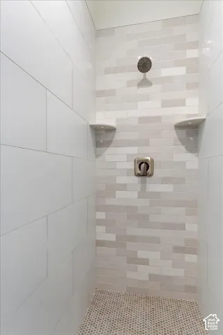 Shower featuring large-format white wall tile, a linear brick-patterned tile accent wall, integrated corner shelving, a circular shower head, and mosaic tile flooring