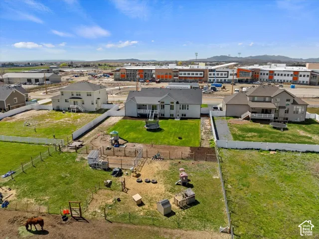 Aerial perspective of a multi-level suburban residence featuring a rear deck, a fenced yard with grass and earth-covered sections, and mountain silhouettes in the distance