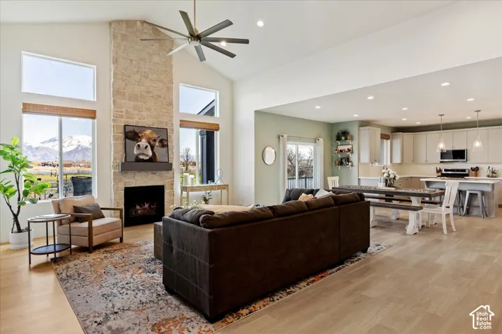 Vaulted ceiling featuring a floor-to-ceiling stone fireplace, expansive multi-pane windows, wood-finish flooring, and recessed lighting