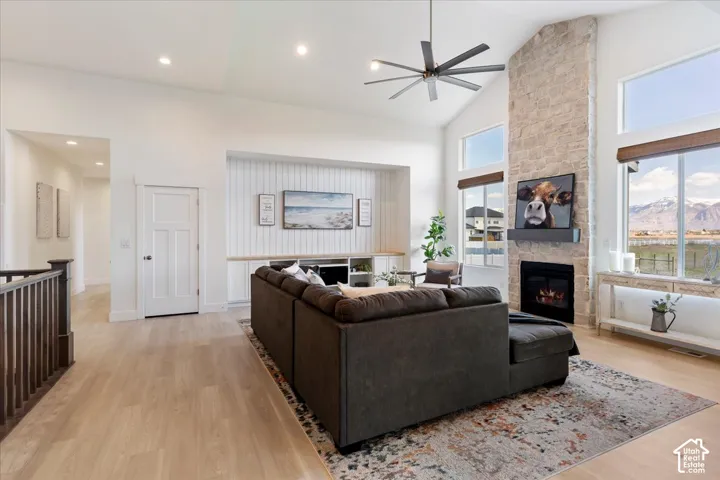 Vaulted ceilings featuring a large-scale ceiling fan, floor-to-ceiling stone fireplace, wood-finish flooring, and built-in cabinetry with vertical paneling
