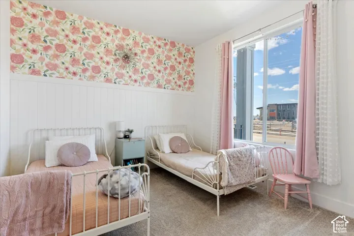 Room featuring floral wallpaper, white vertical wainscoting, wall-to-wall carpeting, and a large window