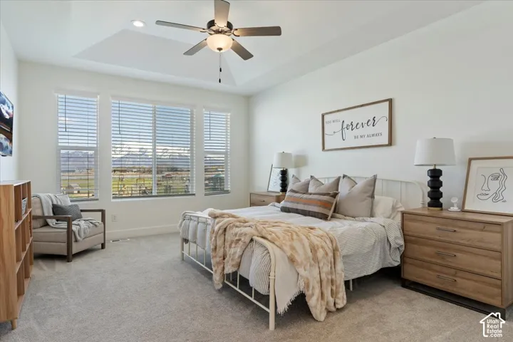 Tray ceiling featuring a central multi-blade ceiling fan with integrated lighting, expansive windows with mountain scenery, and neutral carpeting