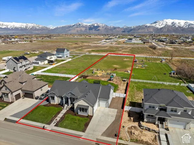 Aerial perspective of a multi-gabled residence featuring a light-toned brick facade, an asphalt shingle roof, a multi-car garage, and a concrete driveway, set against a backdrop of mountain ranges