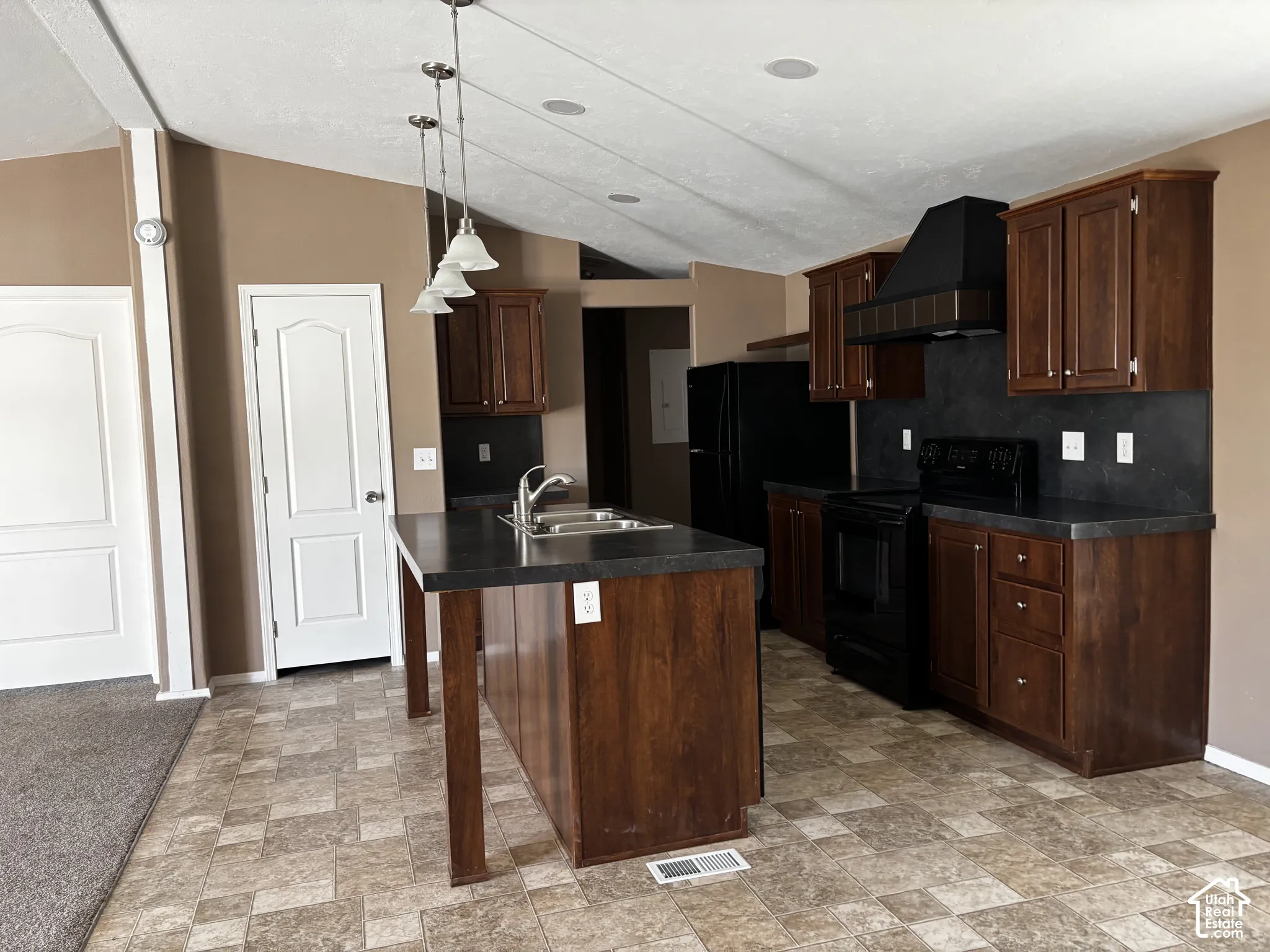 Kitchen featuring dark wood cabinetry, a center island with a dual-basin stainless steel sink, solid surface countertops, black appliances, and pendant lighting