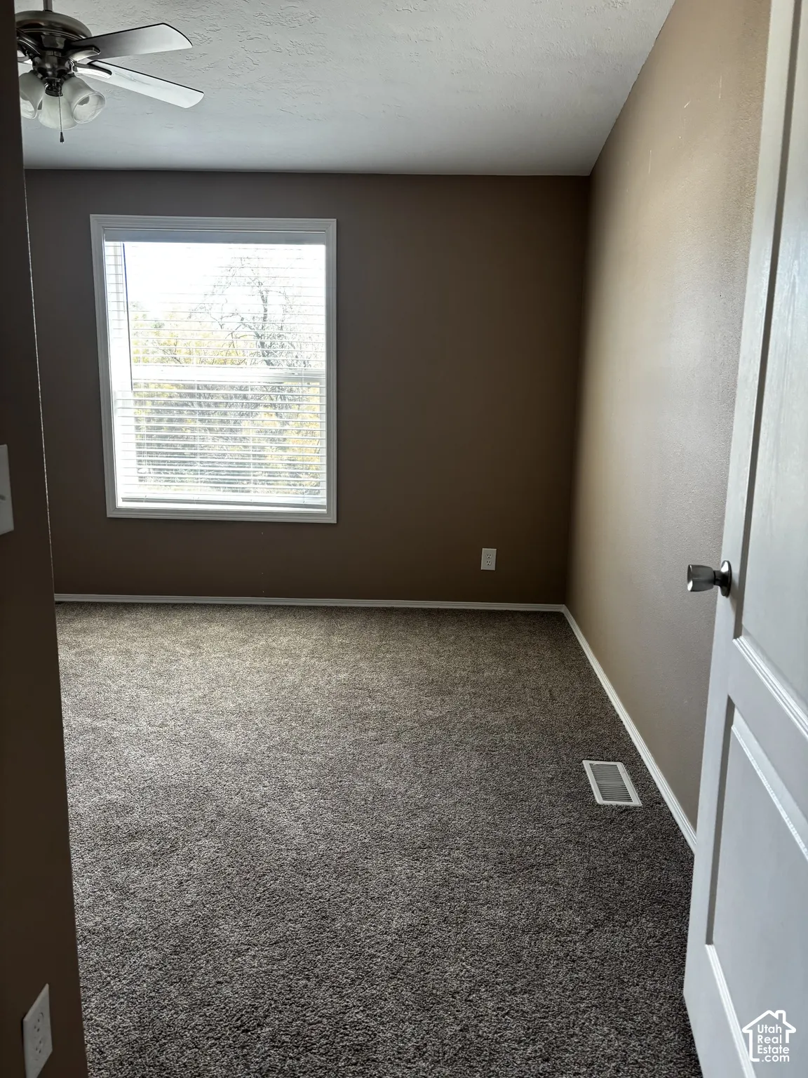 Neutral-toned interior featuring wall-to-wall carpeting, a multi-pane window, and a ceiling fan with integrated lighting