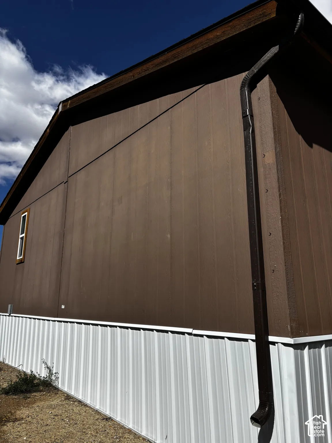 Exterior elevation featuring vertical paneled siding, a contrasting corrugated metal base, and an attached downspout system