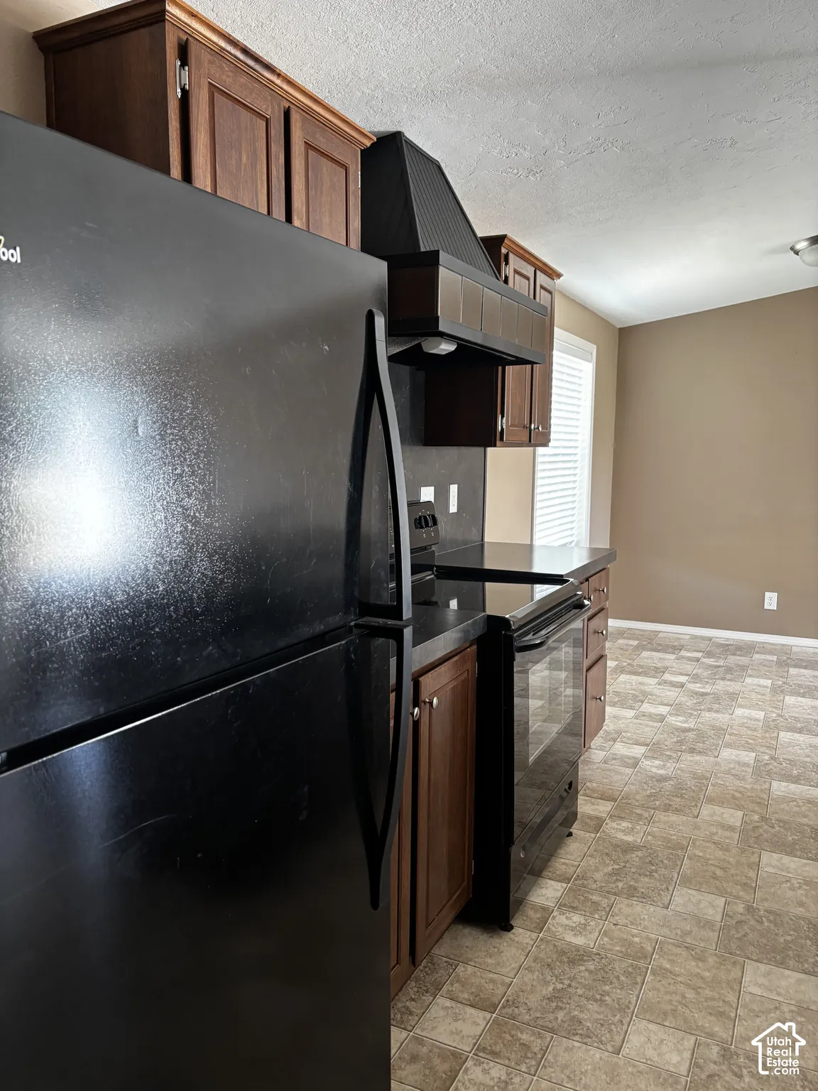Kitchen featuring wood cabinetry, black appliances, tile backsplash, and stone-patterned flooring