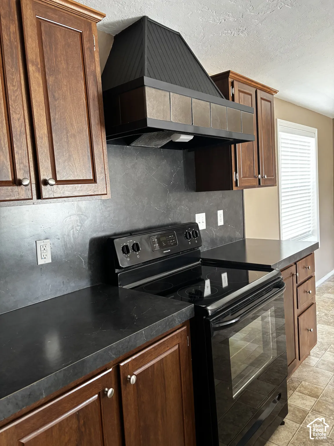 Kitchen featuring stained wood cabinetry, solid-surface countertops, full-height backsplash, and a custom range hood with tiled trim