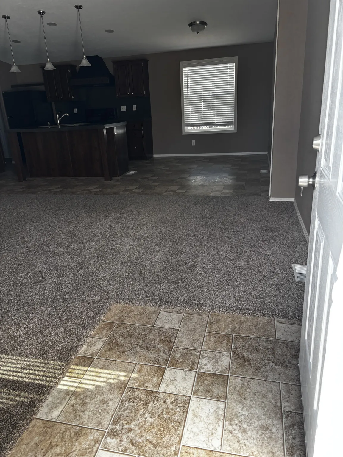 Entryway featuring ceramic tile flooring, neutral wall-to-wall carpeting, kitchen island with built-in cabinetry, and overhead pendant lighting