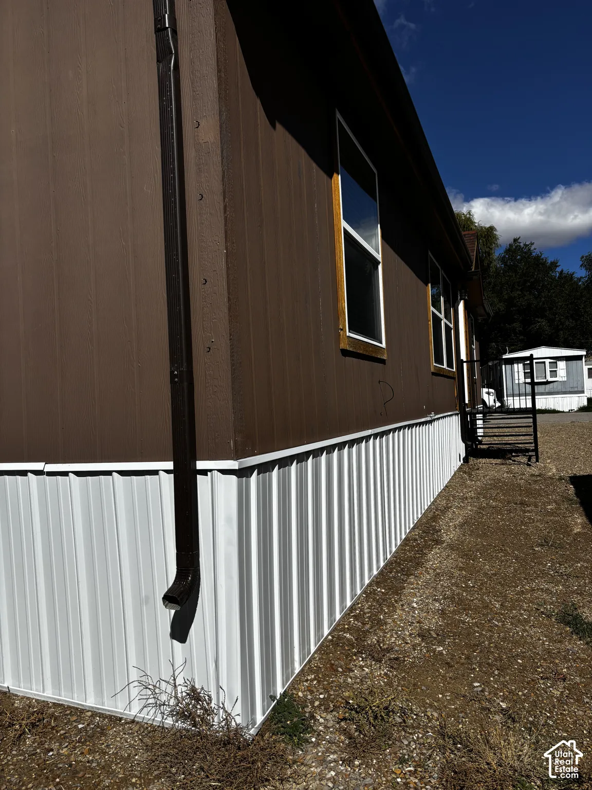 Exterior featuring brown vertical siding, white corrugated metal skirting, and dark-framed windows