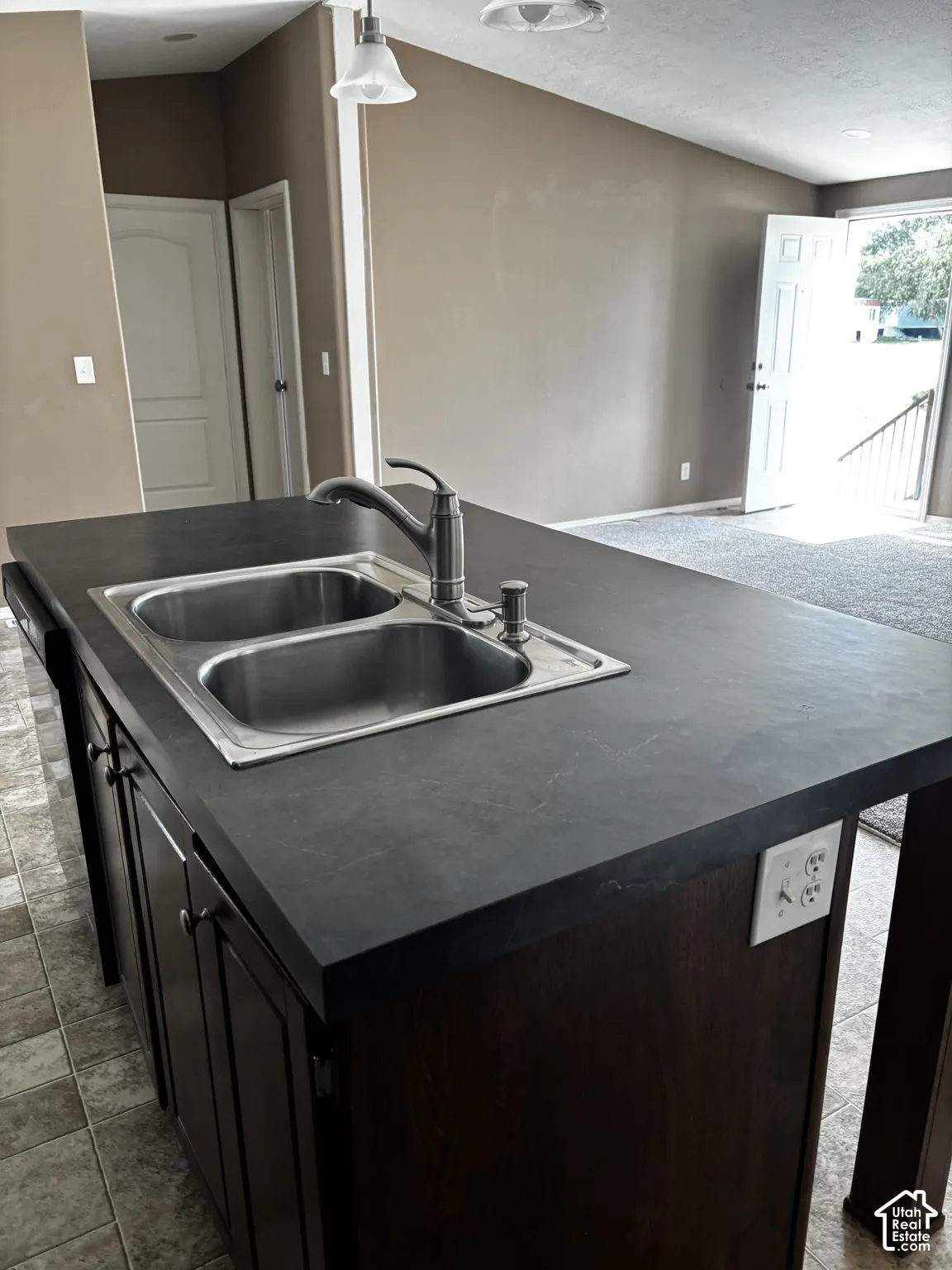 Kitchen island featuring dark-finish cabinetry, matte-finish countertop, dual-basin stainless steel sink, and gooseneck faucet