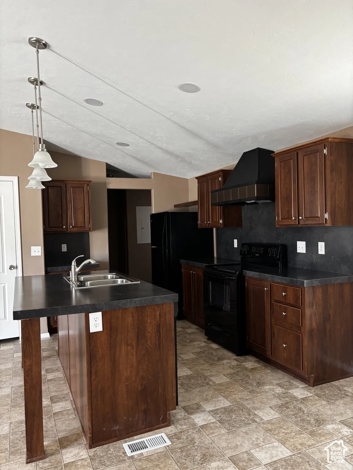 Kitchen featuring dark wood-finish cabinetry, a contrasting center island with a dual-basin stainless steel sink, solid-surface countertops, and a coordinated black range hood