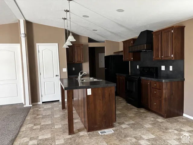 Kitchen featuring dark wood cabinetry, a center island with a dual-basin stainless steel sink, solid surface countertops, black appliances, and pendant lighting