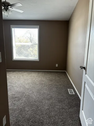 Neutral-toned interior featuring wall-to-wall carpeting, a multi-pane window, and a ceiling fan with integrated lighting