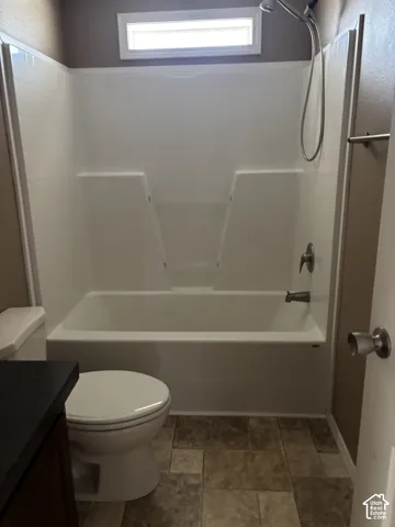 Bathroom featuring a white tub-shower combination with a hand-held showerhead, transom window, and stone-finish tile flooring