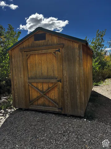 Exterior storage structure featuring wood-panel construction, gable roofline, and metal strap hinges