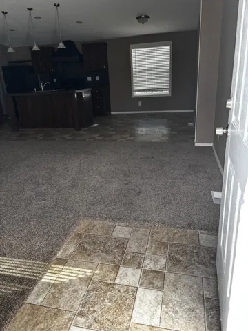 Entryway featuring ceramic tile flooring, neutral wall-to-wall carpeting, kitchen island with built-in cabinetry, and overhead pendant lighting