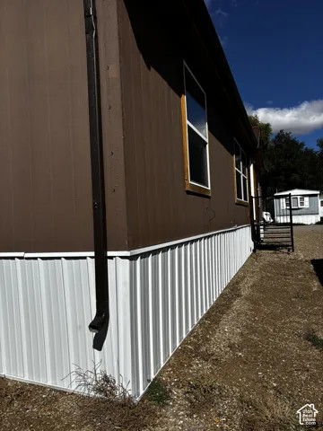 Exterior featuring brown vertical siding, white corrugated metal skirting, and dark-framed windows