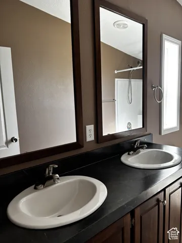 Dual vanity featuring dark cabinetry, dark solid-surface countertops, integrated oval basins, chrome-finish faucets, and framed wall mirrors
