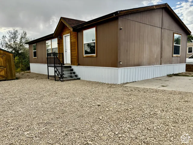 Exterior featuring brown panel siding, white skirting, dual-tone facade accents, metal stairs with handrails, and a gravel surface