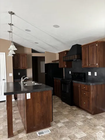 Kitchen featuring dark wood-finish cabinetry, a contrasting center island with a dual-basin stainless steel sink, solid-surface countertops, and a coordinated black range hood