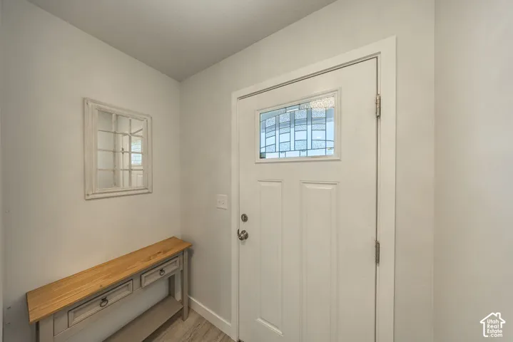 Entryway featuring a white door with a decorative glass panel, wood-finish flooring, and a wall-mounted rectangular mirror