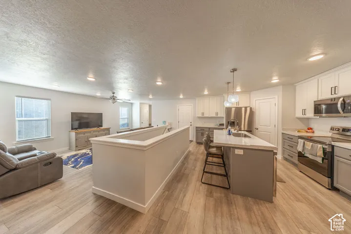Open concept space featuring wood-finish flooring, recessed lighting, kitchen island with stone-surface countertop, dual-tone cabinetry, and stainless-steel appliances