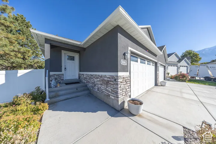 Exterior featuring dark stucco siding, stone veneer accents, white trim, a multi-car garage, and concrete entry steps