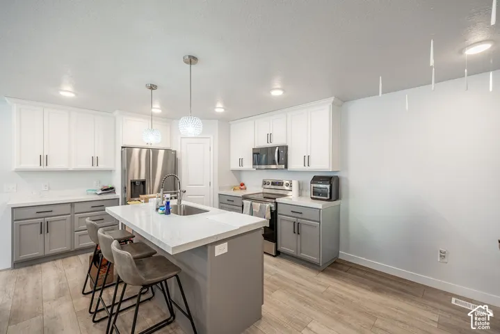 Kitchen featuring two-tone cabinetry, quartz countertops, a central island with a stainless steel sink, stainless steel appliances, and wood-finish flooring