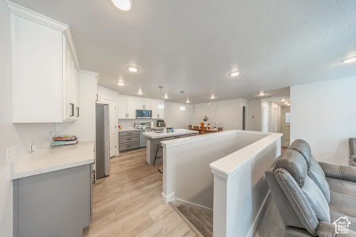 Kitchen featuring white upper cabinetry, grey lower cabinetry, central island with seating, stone-finish countertops, and wood-finish flooring