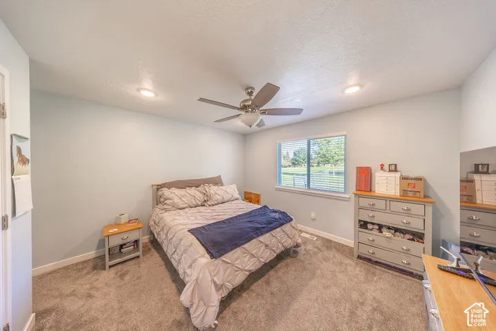 Neutral-toned wall-to-wall carpeting, recessed ceiling lighting, a brushed-metal ceiling fan with an integrated light fixture, and a large horizontal sliding window