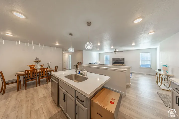 Kitchen featuring a central island with a stone-surface countertop, stainless steel undermount sink, gray cabinetry, recessed lighting, and pendant illumination