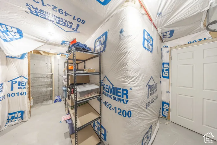 Unfinished storage area featuring concrete flooring, insulated walls, and a white six-panel door