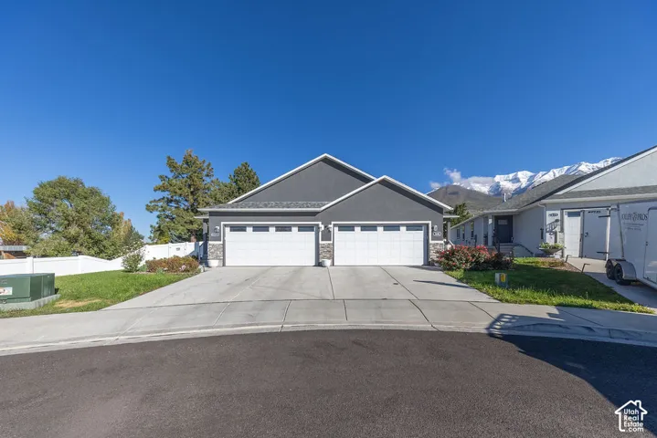 Exterior featuring dual-car garage bays, stone veneer accents, concrete driveway, white vinyl perimeter fencing, and mountain backdrop