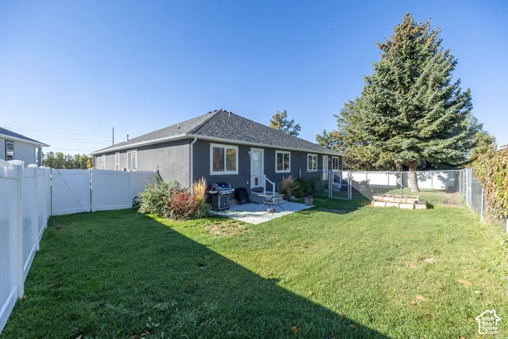 Rear exterior featuring stucco siding, a shingled roof, concrete patio, privacy fencing, and mature evergreen trees