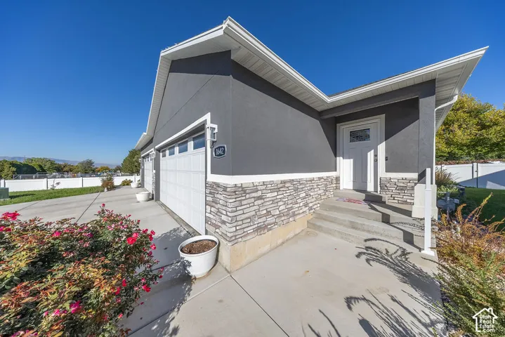 Exterior featuring dark stucco siding, stacked stone veneer, white trim, a multi-car garage, and a covered entryway