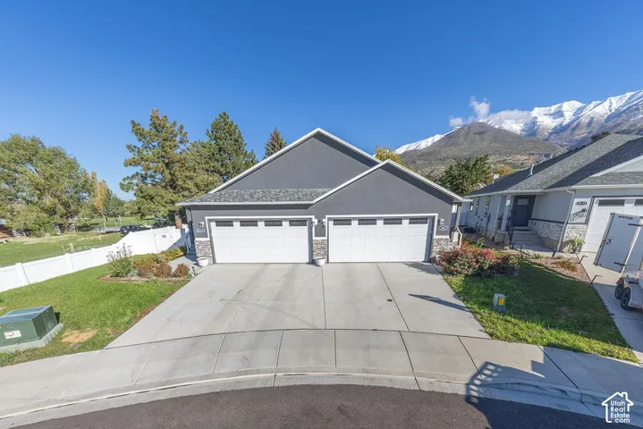 Three-car garage exterior featuring stone veneer accents, multi-pane garage doors, asphalt shingle roofing, and a concrete driveway, set against a mountainous landscape